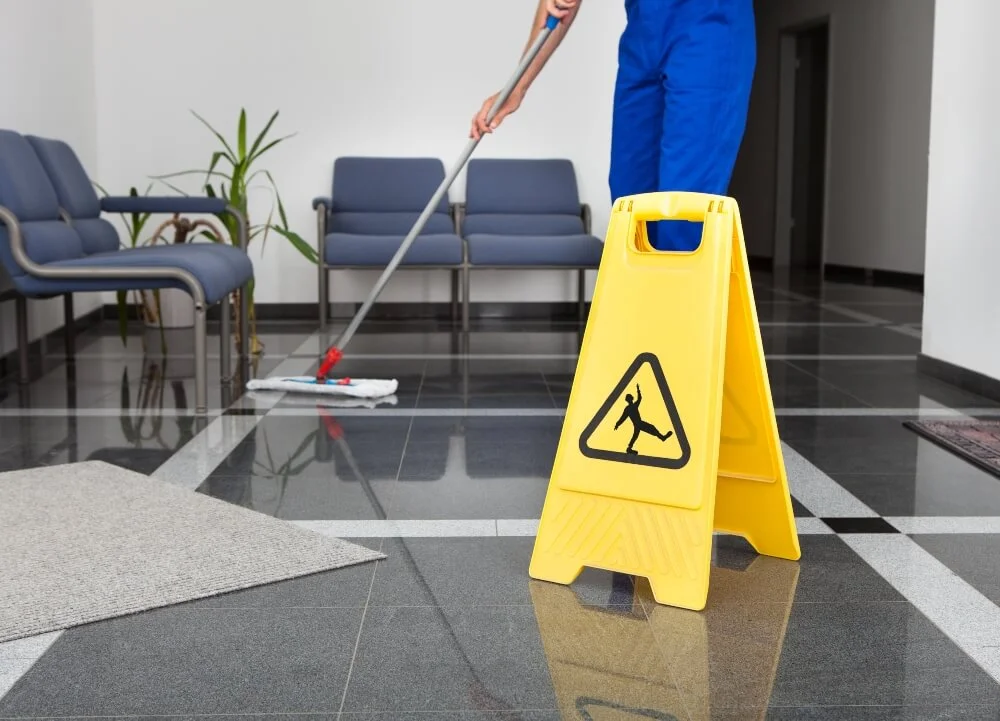 A cleaner mopping the office floor and placed a slip hazard sign